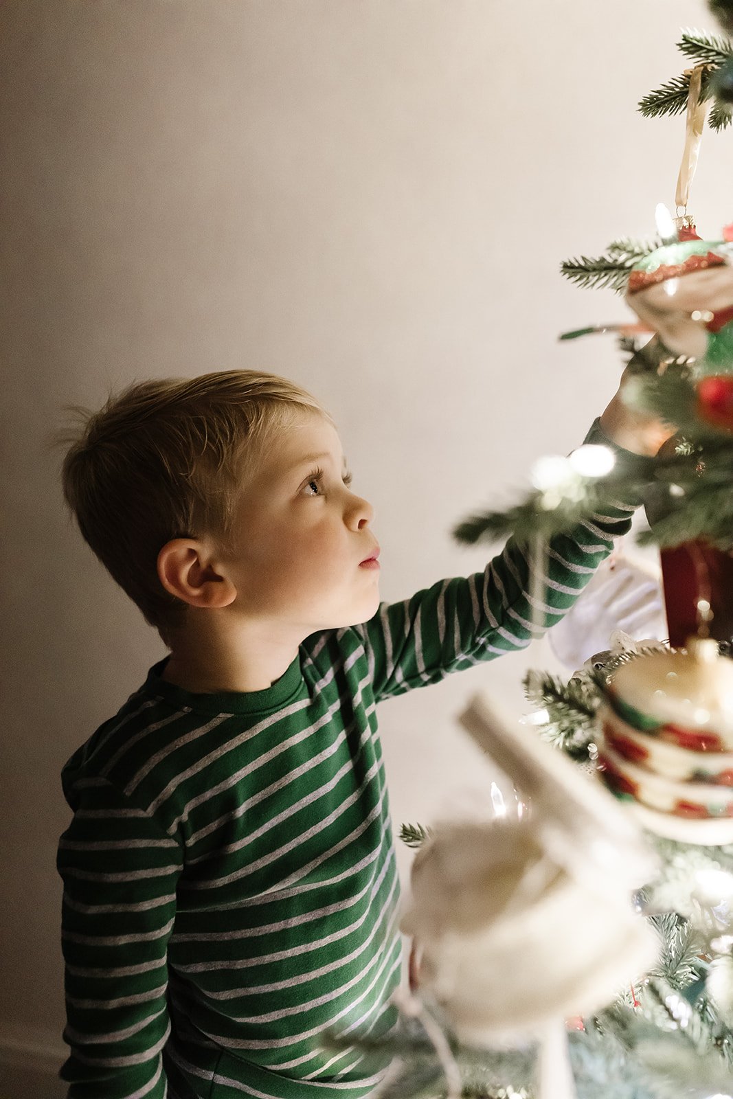 Little boy in front of the Christmas tree where green striped pajamas