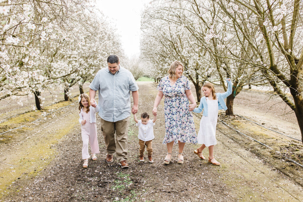 family dressed in spring colors walking through an almond orchard. Spring Family photos outfits ideas.