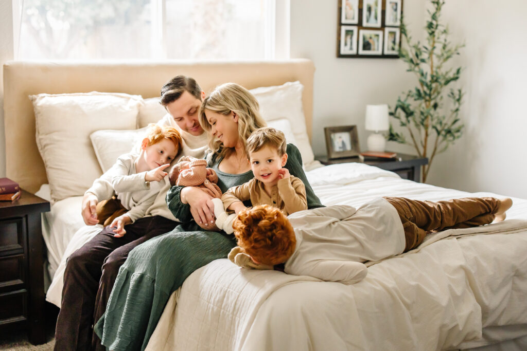 Family snuggling on a bedf with a newborn, emphasizing comfort and connection at an in-home newborn photo session. 
